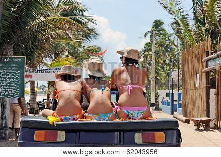 Three women with different heights wearing bikinis and hats, sitting on a buggy.