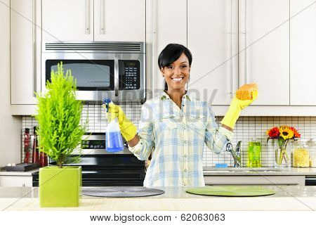 Smiling young black woman with sponge and rubber gloves cleaning kitchen