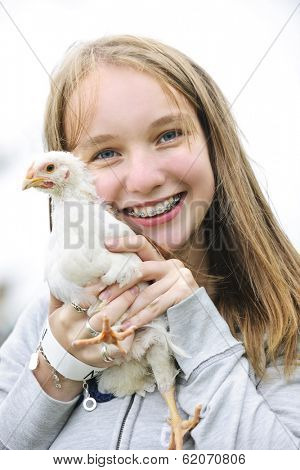 Smiling teenage girl with braces holding young chicken