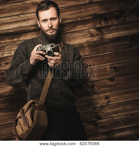 Handsome man wearing cardigan with vintage camera in wooden house interior 