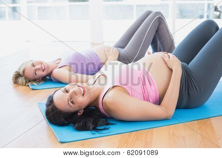 Smiling pregnant women in yoga class lying on mats in a fitness studio