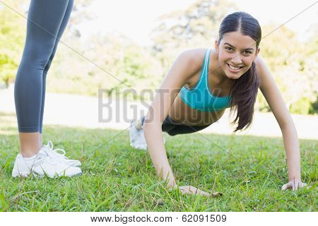 Portrait of smiling woman doing push ups in park with friend standing by her