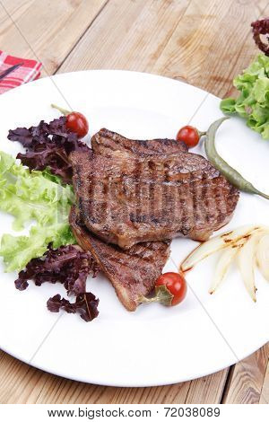 meat food : roast steak boneless with roast onion and red hot peppers, served on green lettuce salad on dish isolated over wooden table