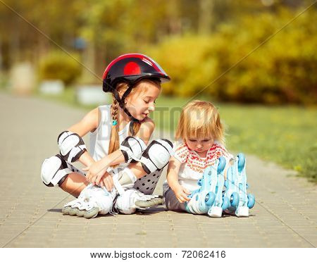 two little sisters in a roller skates and  helmet sitting  on the street