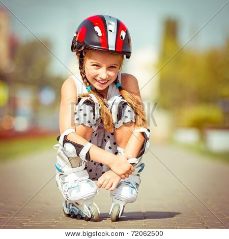 Little girl in roller skates sitting on a city street