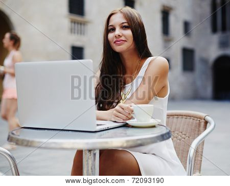 Smiling young woman is using a laptop in sidewalk cafe