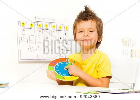 Smiling boy holding colorful carton clock sitting