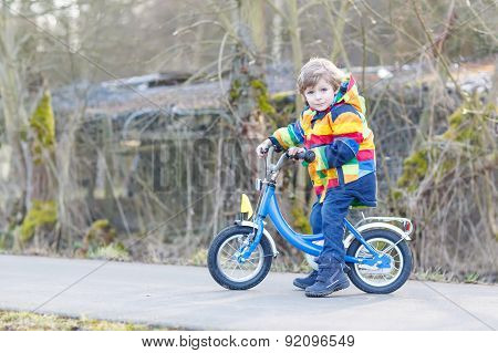 Kid Boy In Safety Helmet And Colorful Raincoat Riding Bike, Outdoors.