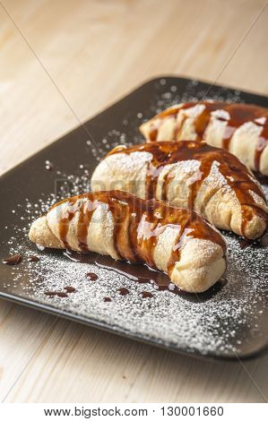 Puffs on brown plate with chocolate glaze and sugar powder. Selective focus