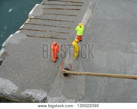 ISLAND OF ANDROS, CYCLADES, GREECE - SEPTEMBER 12, 2009: Three dock workers in wet work protective suit standing on the dock waiting for permission to release ship mooring ropes