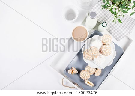 Cookies on white and gray plate with cups of coffee and bottles of milk on white shutters background with green and white flower top view