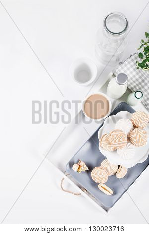 Cookies on white and gray plate with cups of coffee and bottles of milk on white shutters background with green and white flower top view