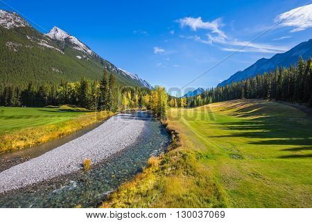 Magnificent valley in Banff National Park. Beneaped autumn stream with a pebbly bottom flows among fields and pine forests