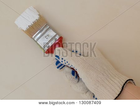 hand with brush in white paint near the wall