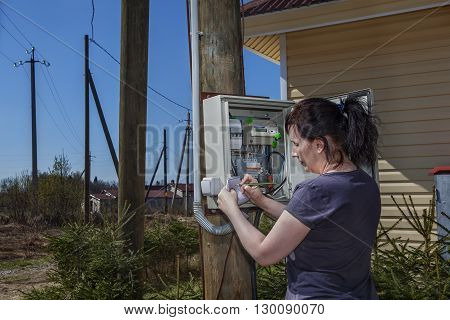 Peasant Woman looking electric meter data in switchgear mounted on a wooden pole near farm house in countryside.
