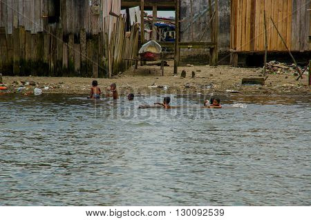 Muisne, Ecuador - March 16, 2016: Muisne town beach very polluted, local kids swimming and enjoying the water.