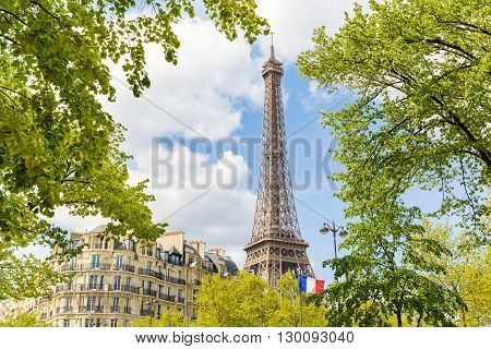 Paris view with the Eiffel Tower a French flag some trees and a typical Parisian building. Travel and architecture concepts about the capital city of France.