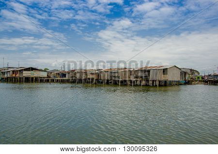 Muisne, Ecuador - March 16, 2016: Muisne town as seen from water, modest wooden houses sitting on poles waterfront pacific ocean, city buildings background and beautiful blue sky.