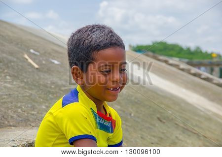 Muisne, Ecuador - March 16, 2016: Kid sitting outdoors with yellow football shirt on and smiling.