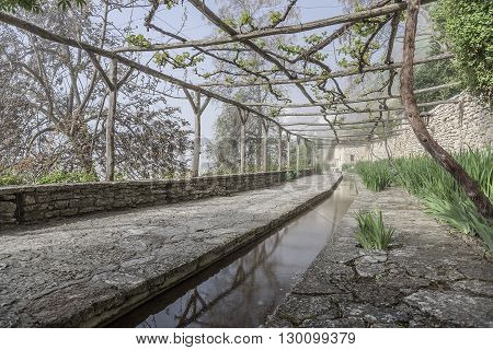 Old stone orangery with water channel and a vineyard.