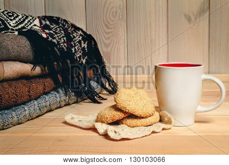 Pile knitted sweater, cup and cookies on a wooden background