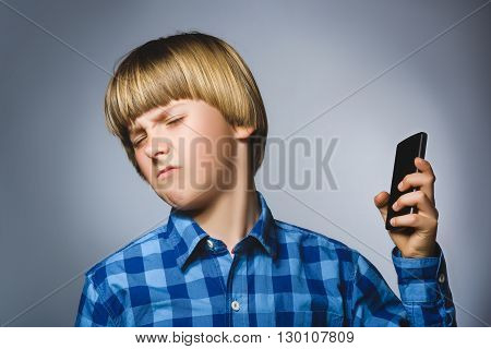Closeup Portrait of worried stressed boy with mobile going irritation on gray background.
