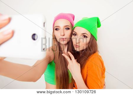 Beautiful Hipster Sisters In Caps Taking Photo On Mobile Phone