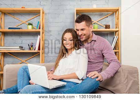 Happy Couple In Love Sitting On The Sofa With Laptop And Doing Shopping