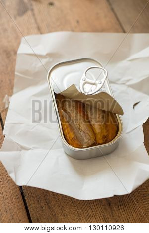 A slightly opened can of sardines or herring in oil on a piece of paper
