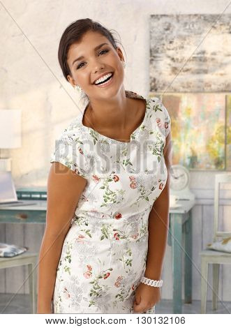 Attractive caucasian young brunette smiling lady at vintage home. Standing, wearing colorful dress, looking at camera, toothy smile.