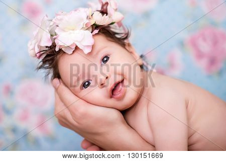 Portrait of a baby girl with a wreath of pink flowers on her head on a light background