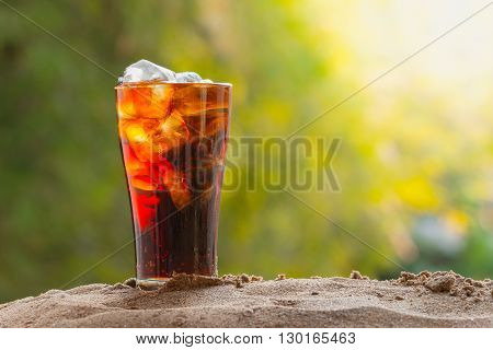 cola with in glass with ice cubes on sand nature background