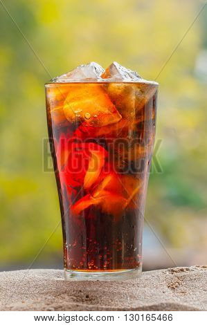 cola with in glass with ice cubes on sand nature background