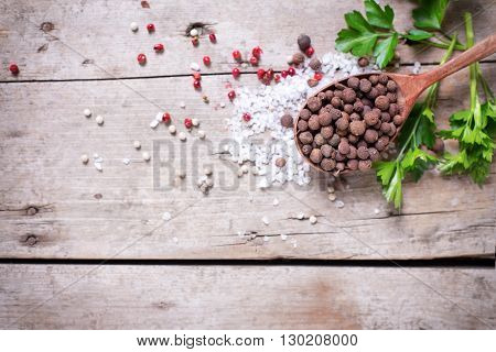 Seasoning for cooking. Allspice pepper in wooden spoon and sea salt red pepper and herb parsley on aged wooden background. Food ingredient. Selective focus. Place for text. Flat lay. Top view.