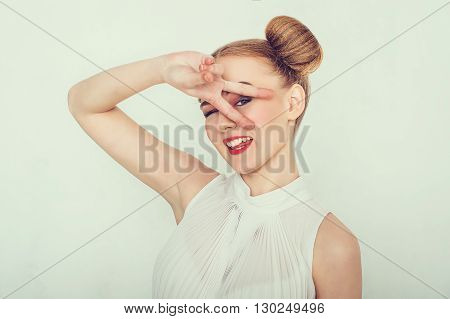 Beautiful girl with funny hairstyle makes peace sign hands smiling and showing tongue.