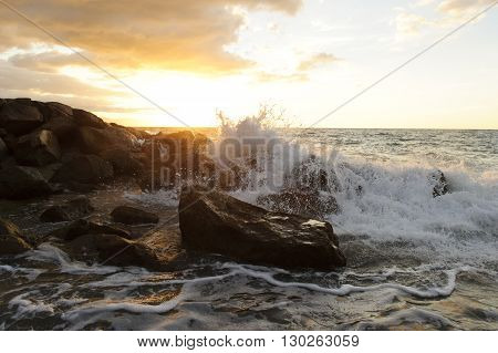 Waves crashing is an ocean seascape with a wave crashing up against a rock throwing water into the air.
