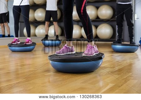 Low Section Of Friends Standing On Bosu Ball In Gym