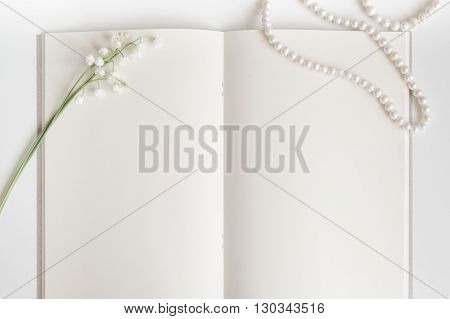 empty vintage book page with chic pearls decoration and lily of the valley background with copy space