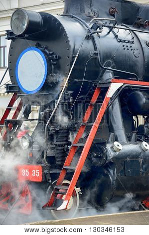 LVIV UKRAINE - DECEMBER 2015: Old Soviet vintage black retro train L-3535 at the railway station in Lviv produces steam from the pipes