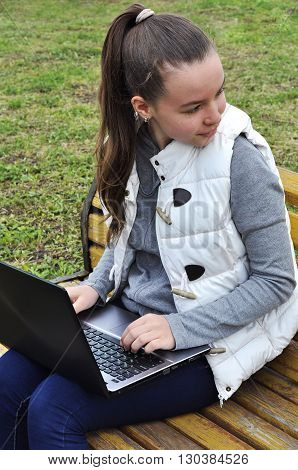 Girl with laptop sitting on a bench in the park