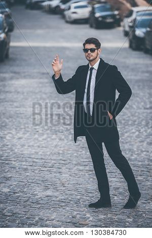 Hey taxi! Full length of handsome young well-dressed man waving for taxi while walking outdoors