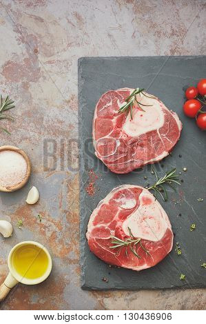 Raw veal shank.  Raw cuting veal shank on stone slate with rosemary and the ingredients  for making Osso Buco.  Overhead view, vintage toned image, blank space