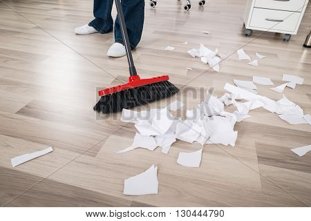 Close-up Of A Janitor Sweeping Torn Paper Pieces On Hardwood Floor