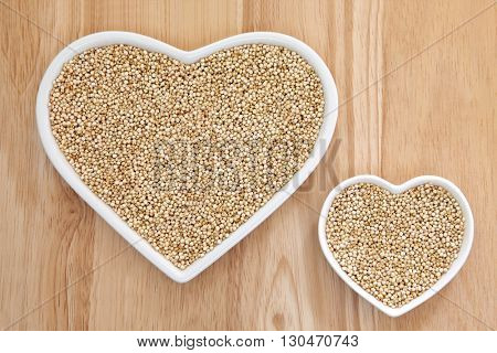 Quinoa grain super food in heart shaped porcelain dishes over beech wood background.
