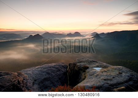 Fantastic dreamy sunrise on the top of the rocky mountain with the view into misty valley