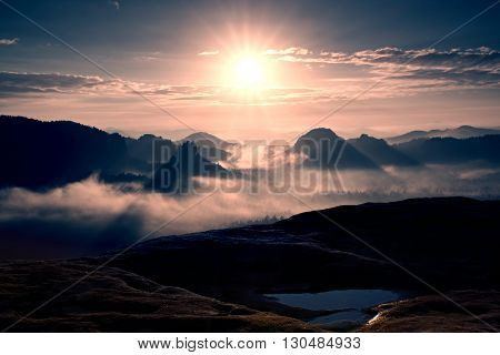 Distant Mountain Range And Heavy Clouds Of Colorful  Mist Above Deep Valleys