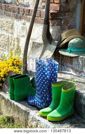 Garden equipment - rubber boots schovels and srtaw hats in sunny day on old stone wall background