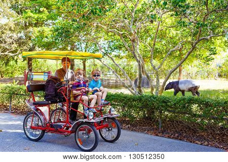 Yound dad and two little kid boys biking on bicycle in zoo. Family with active leisure and watching animals. Father and sons having fun together. Miami zoo, Florida.