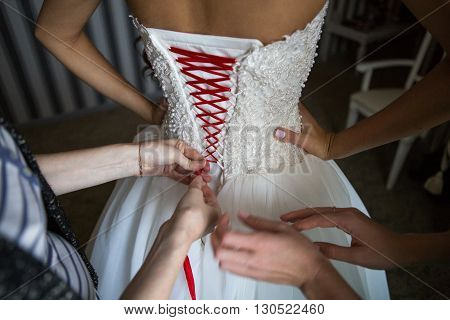 Bride dresses dress in the morning of the wedding day lacing on the back. A closeup image of wedding preparations