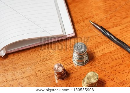 Blank open notebook with pencil and stacks of coins